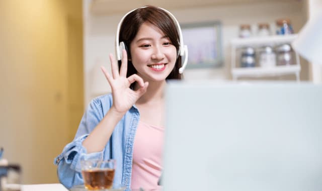 ヘッドホンをつけてノートパソコンの画面をみてOKマークをしめす笑顔の女性